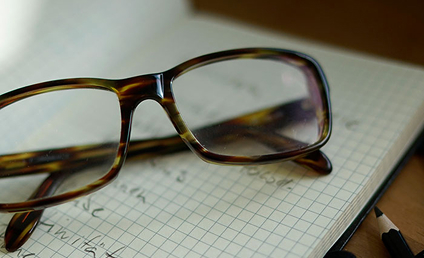Brille liegt auf kariertem Notizblock mit handschriftlichen Notizen und Stift auf Schreibtisch