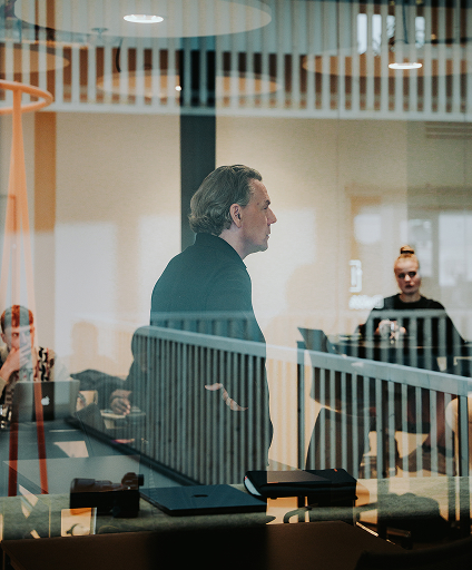 Gesch&auml;ftsmann erkl&auml;rt etwas w&auml;hrend eines Meetings in einem modernen B&uuml;ro mit Team im Hintergrund