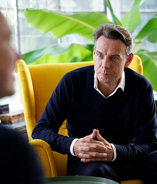 Mann sitzt aufmerksam im gelben Sessel und h&ouml;rt in einer Coaching- oder Beratungssituation zu