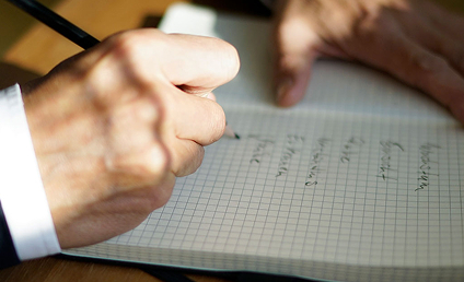Hand schreibt Notizen mit Stift in kariertes Notizbuch auf Schreibtisch
