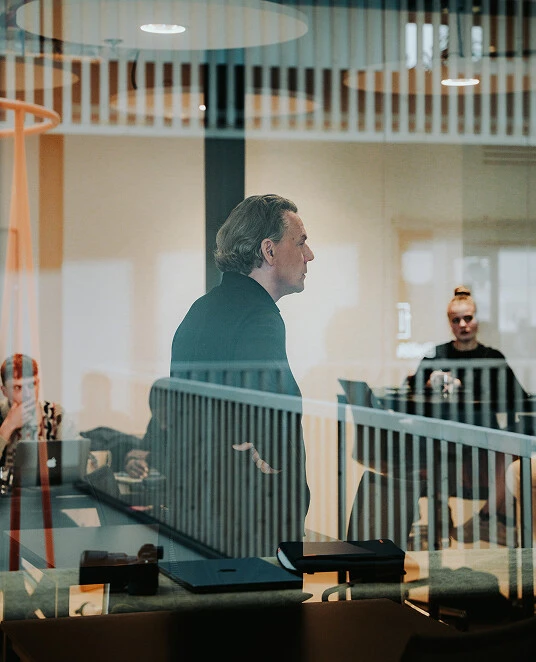 Geschäftsmann erklärt etwas während eines Meetings in einem modernen Büro mit Team im Hintergrund