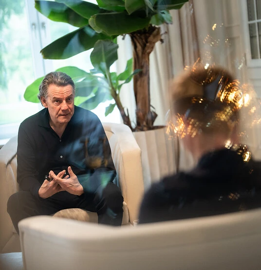 Coach erklärt etwas während eines Beratungsgesprächs mit Klient auf Sofa im hellen Raum