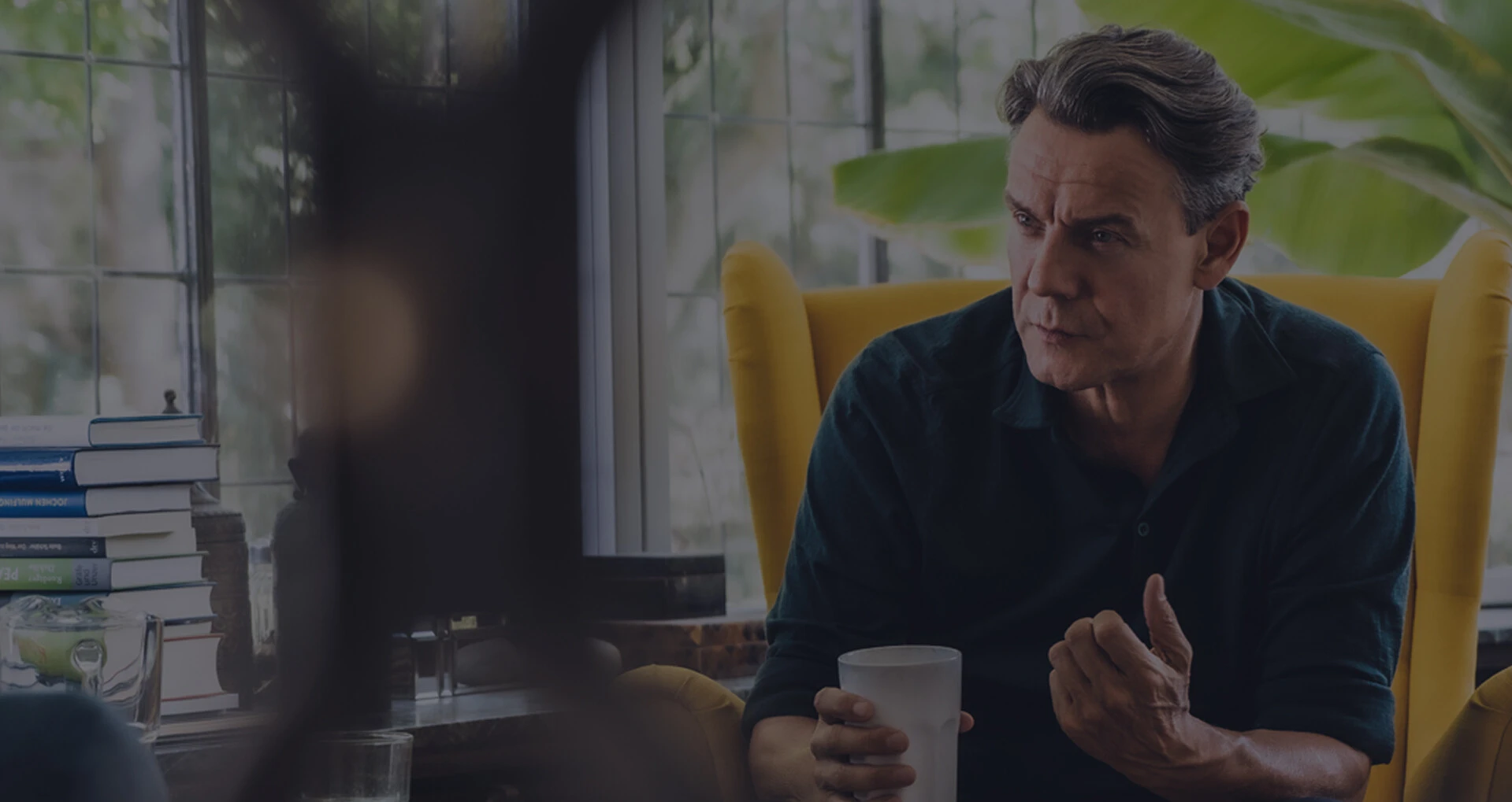 Mann sitzt im gelben Sessel mit Kaffeetasse im Gespräch in heller Wohnraumumgebung