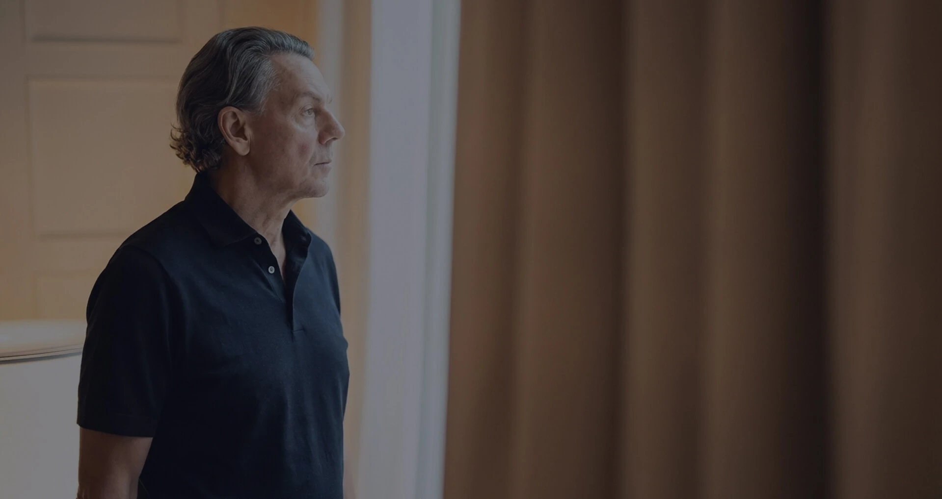 Mann steht nachdenklich am Fenster und blickt nach draußen in ruhiger Atmosphäre