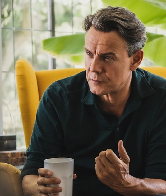 Mann sitzt im gelben Sessel mit Kaffeetasse und hört aufmerksam in einem Gespräch zu