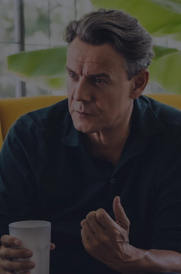 Mann sitzt im gelben Sessel mit Kaffeetasse im Gespräch in heller Wohnraumumgebung